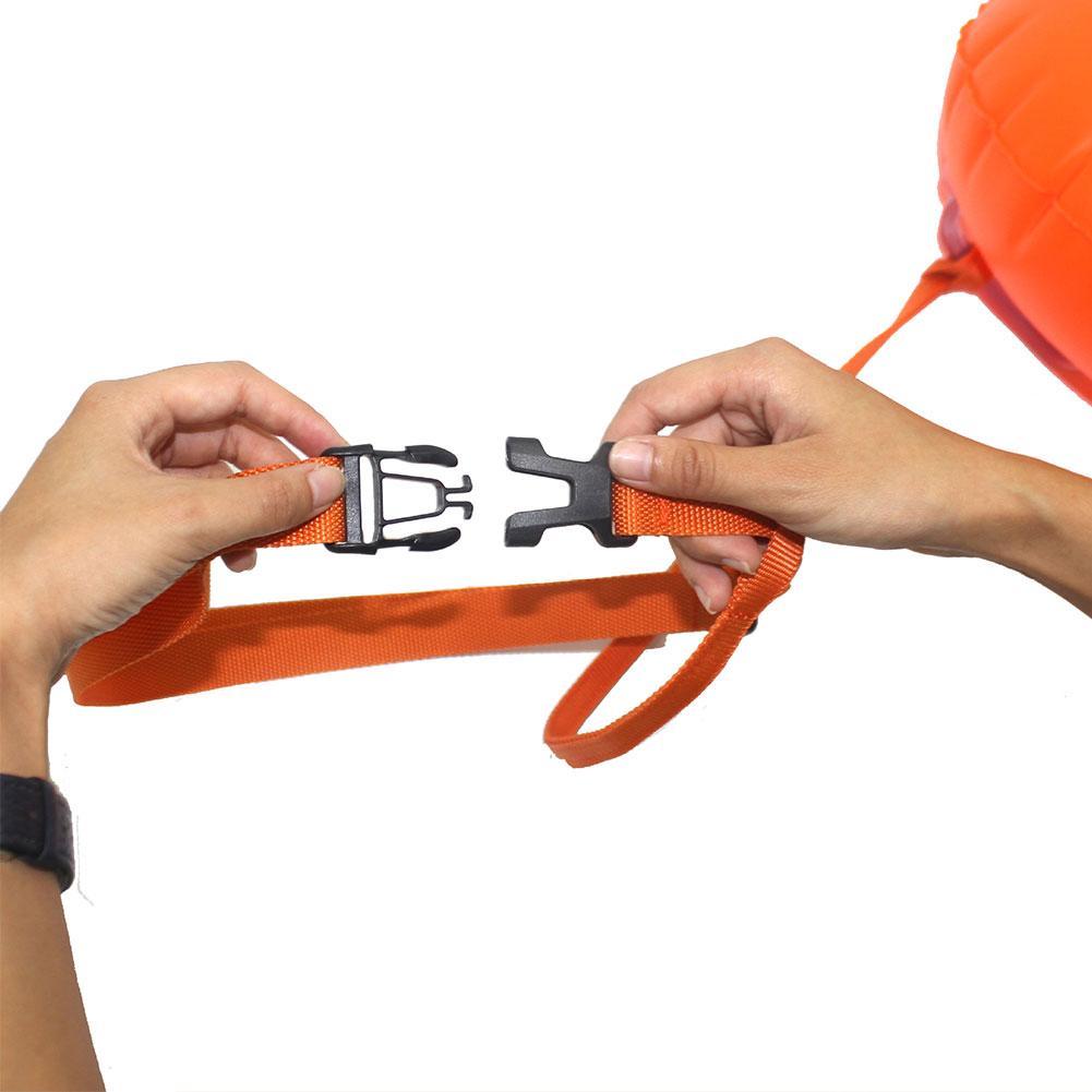 Inflatable swim buoy tow float, orange strap and buckle fasteners held in hands