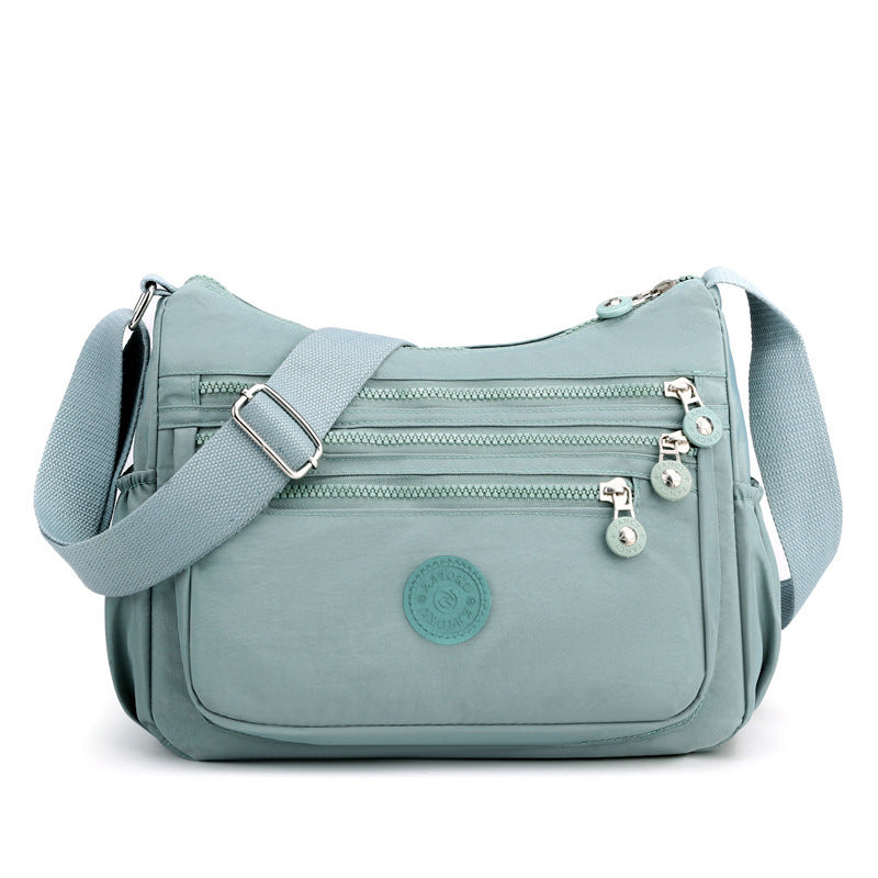 Light blue nylon crossbody bag front view with wide shoulder strap and front zip pockets