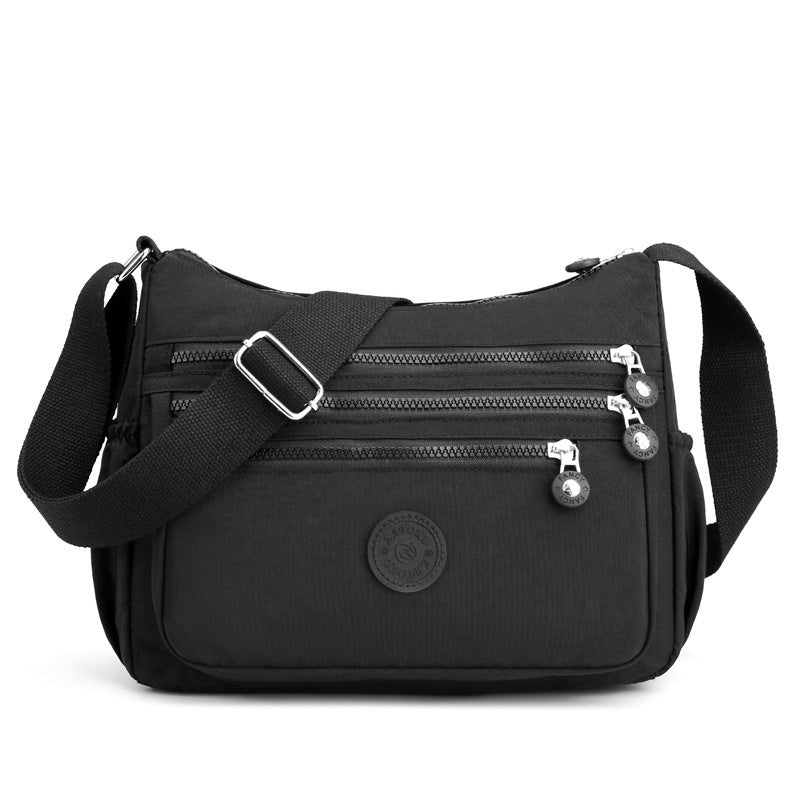 Black nylon crossbody bag front view with front pocket, multiple zippers, and adjustable strap
