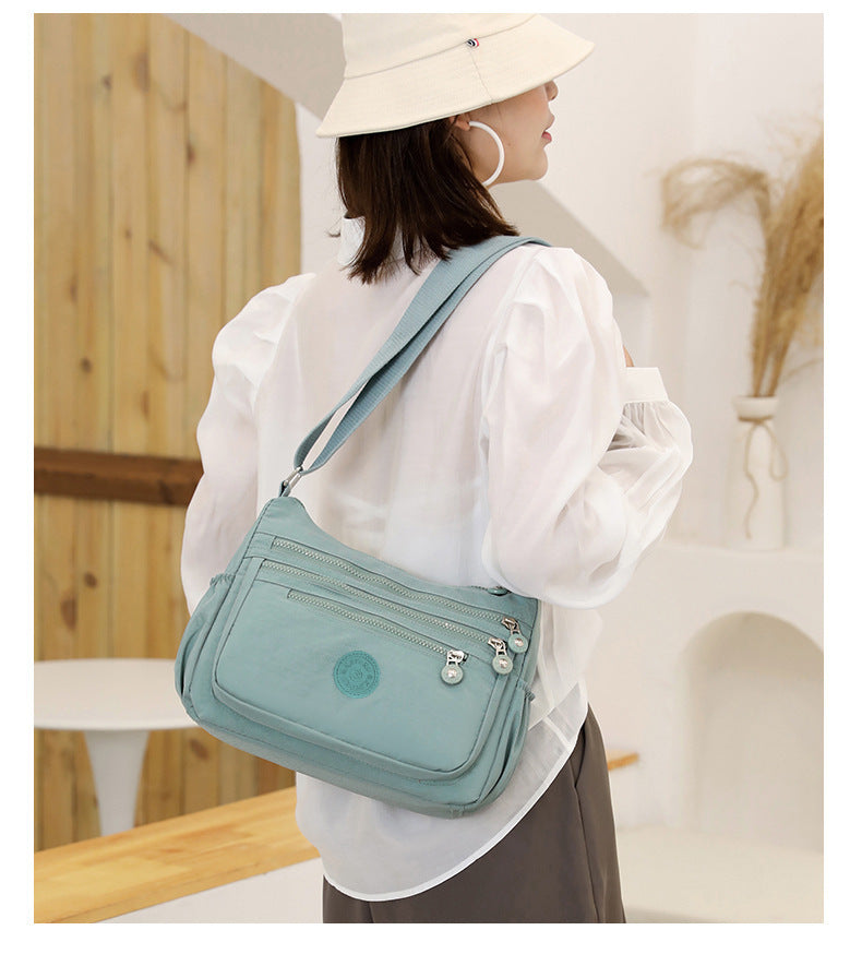 Lightweight multi-layer nylon shoulder bag, water-blue crossbody worn on the shoulder.