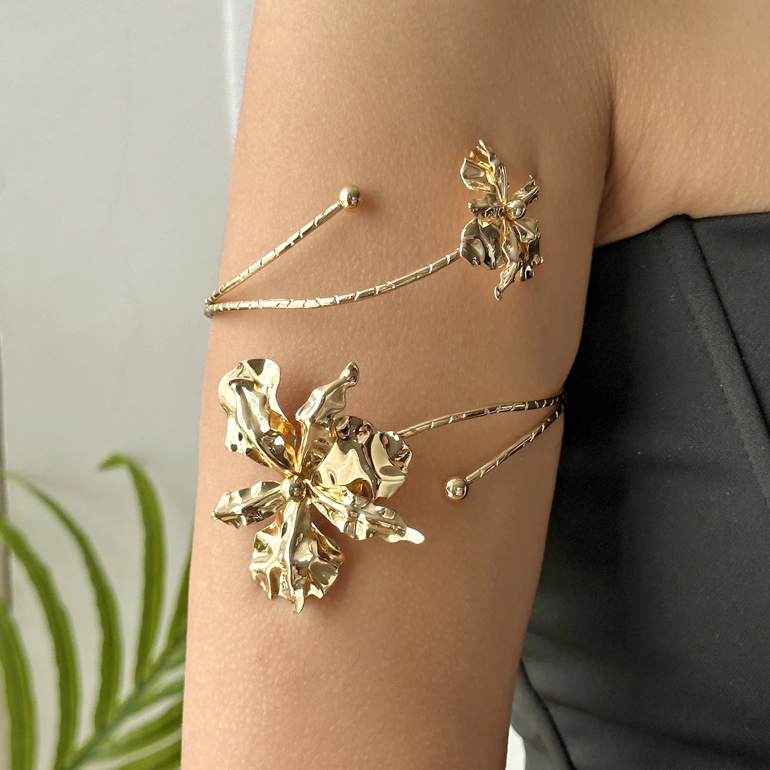 Gold-tone open cuff arm bracelet with large floral charm and small bead accents.