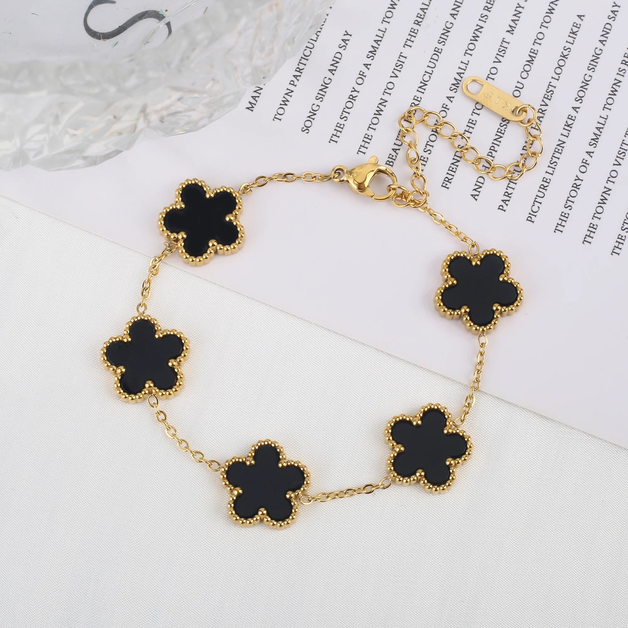 Adjustable gold bracelet with five black clover flower charms and linked chain