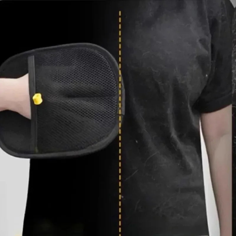 Black pet grooming mitt with mesh texture and yellow tab on a person’s arm