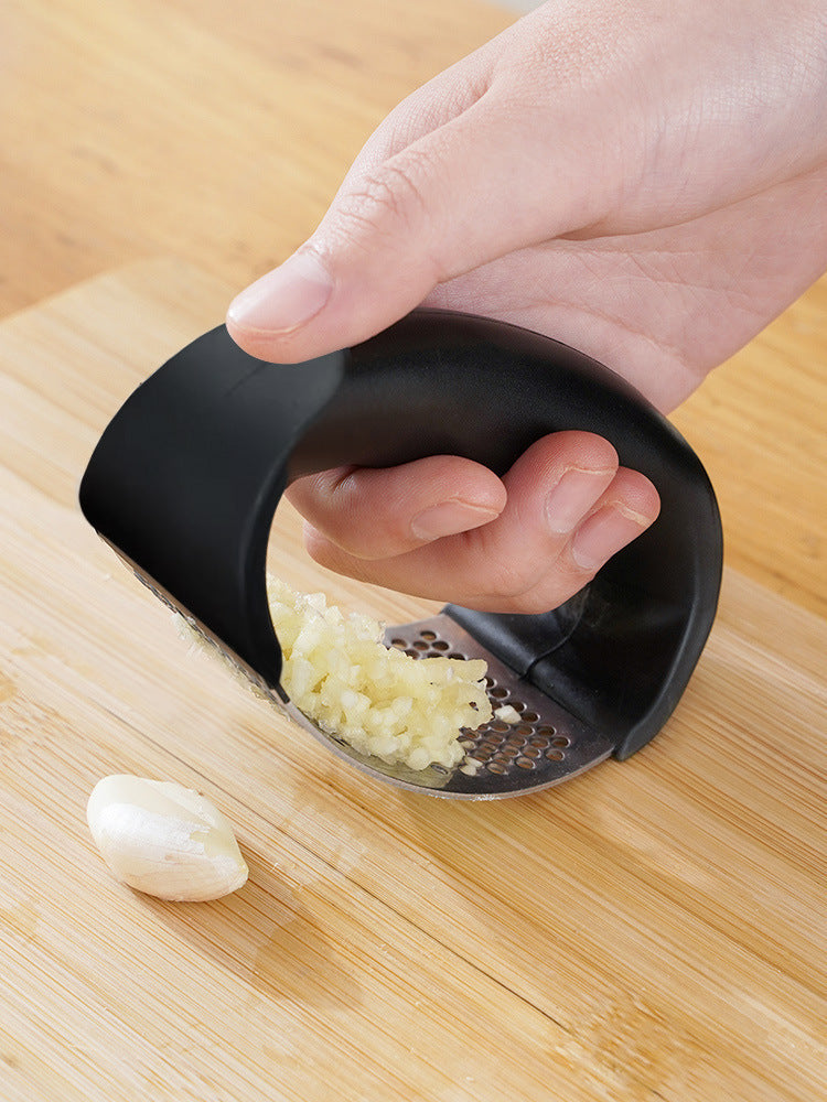 Manual garlic press held by hand, minced garlic visible on perforated plate