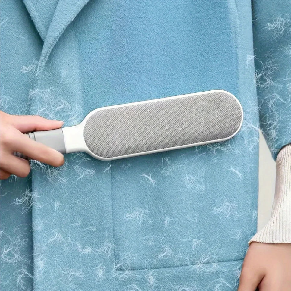 Gray pet hair remover brush with textured pad on blue sweater fabric