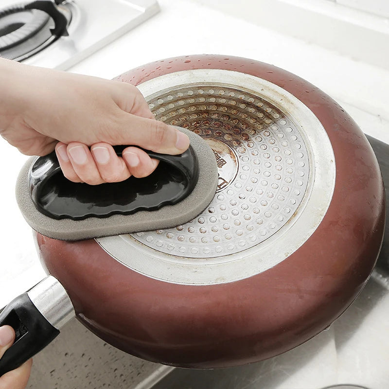 Emery sponge brush cleaner with black handle scrubbing a stovetop pot lid