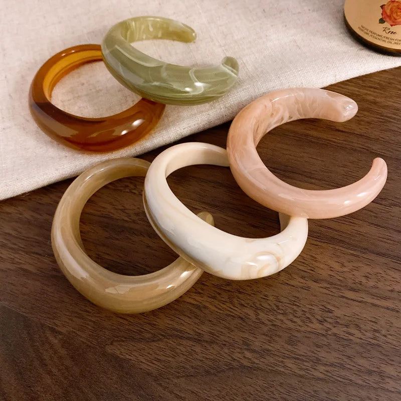 Assorted shiny acrylic open bangles in green, amber, cream, and blush tones