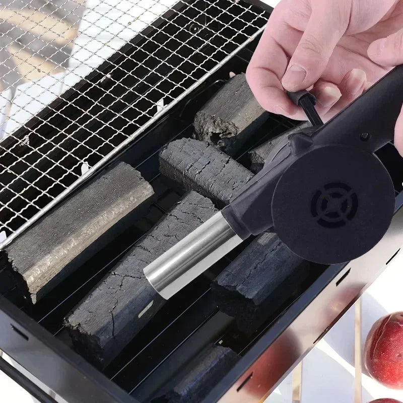 Manual BBQ air blower blowing air over charcoal logs on a grill grate