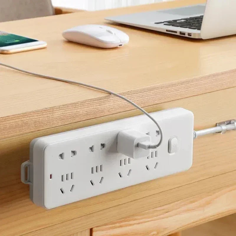Transparent adhesive strips holding a power strip to a wooden tabletop