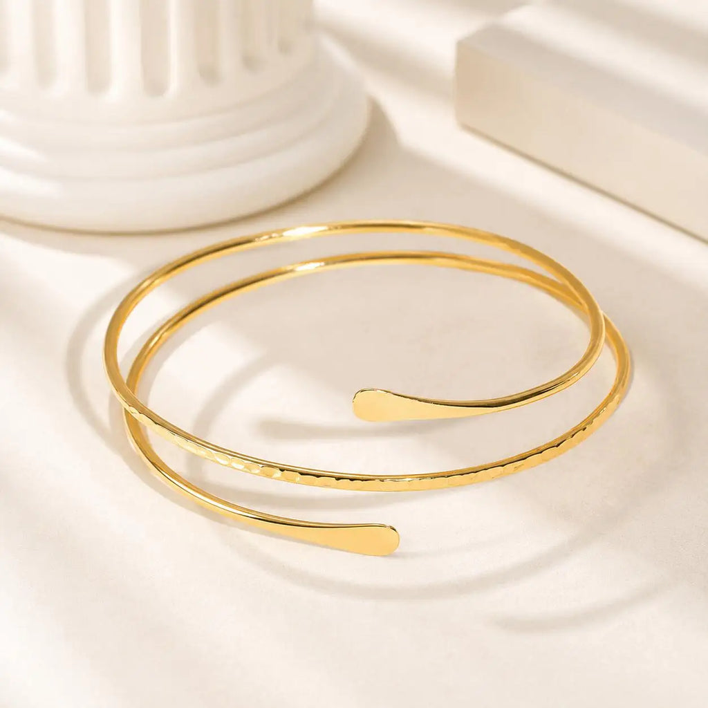 Gold-tone double-wrap arm cuff bracelet with curved bar detail, coiled view