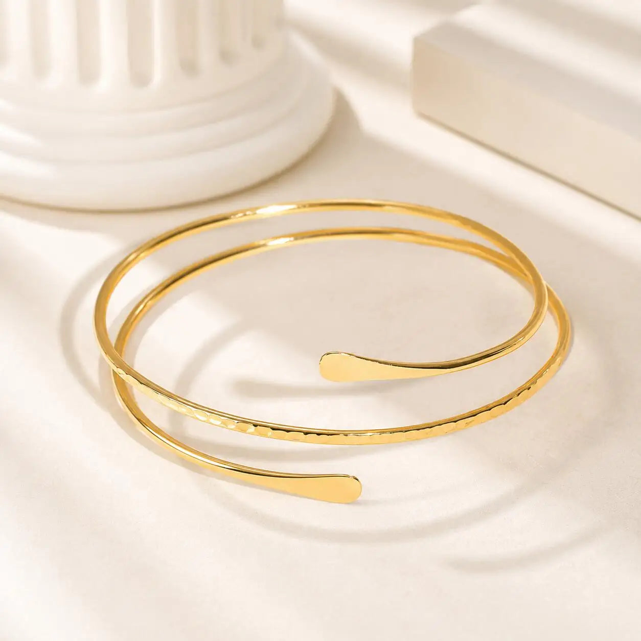 Gold-tone double-wrap arm cuff bracelet with curved bar detail, coiled view