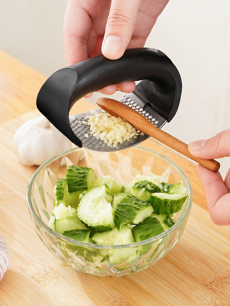 Manual garlic press with black handle crushing garlic over a glass bowl