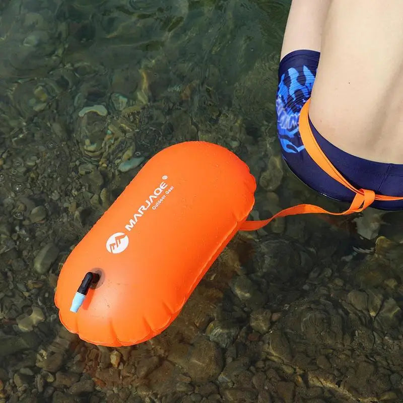 Inflatable swim buoy tow float in orange with strap near swimmer in water