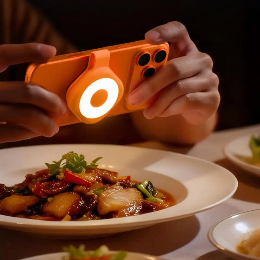 Orange magnetic LED phone light with glowing ring attached to smartphone