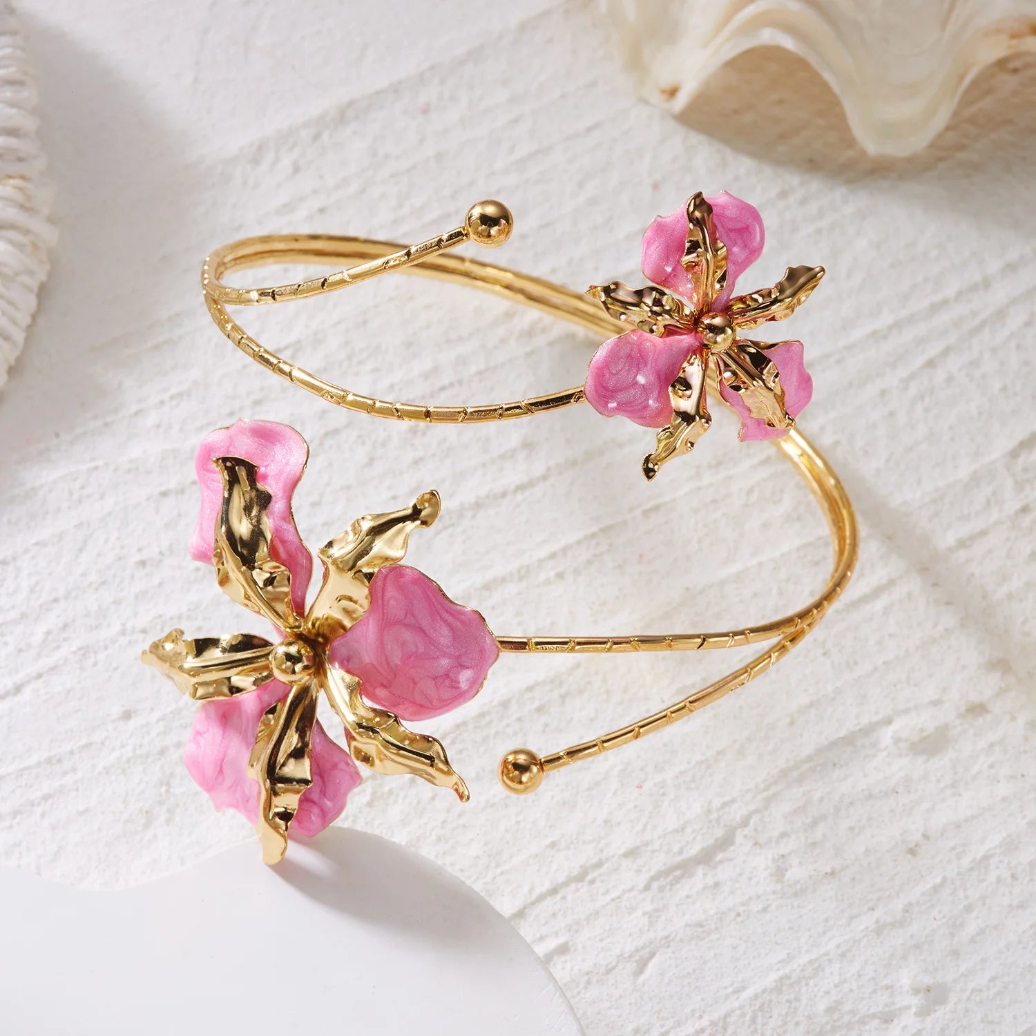 Gold open cuff arm bracelet set with pink enamel flower charms on white fabric