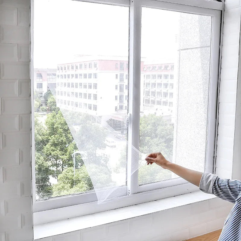 DIY self-adhesive mosquito screen curtain on a window, white mesh with hand adjustment