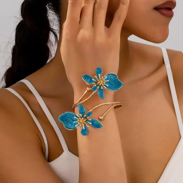 Gold-tone arm bracelet with blue enamel flower charms and dangling bead details.