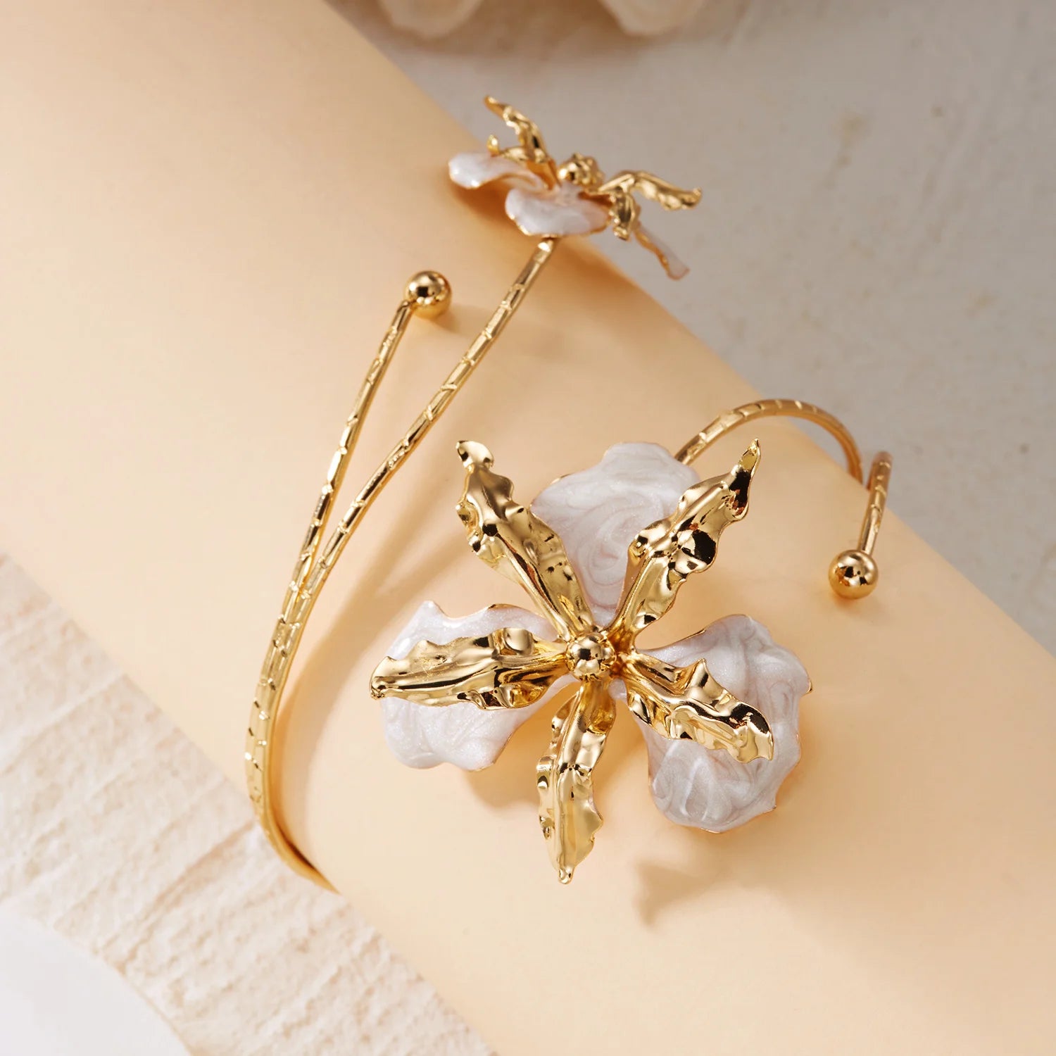 Gold-tone floral arm bracelet with open cuff and white enamel flower cluster.