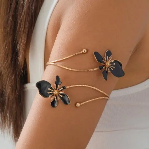 Gold-tone open cuff arm bracelet with dark floral charms and dangling bead accents.
