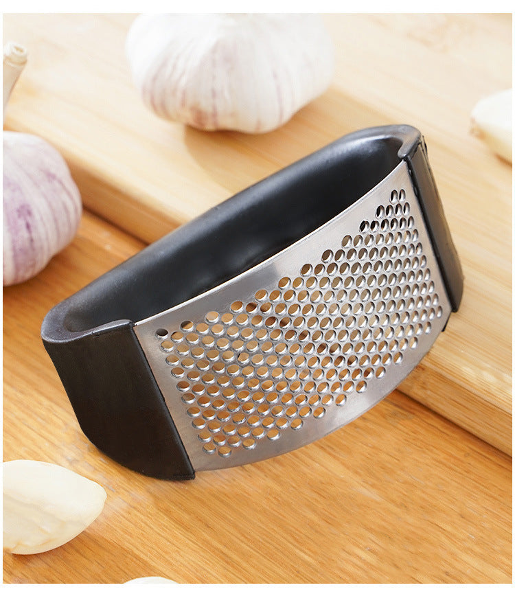 Manual stainless steel garlic mincer with black handle on cutting board