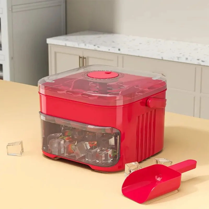 Red ice cube machine with clear window and press lid, with red scoop tool nearby.