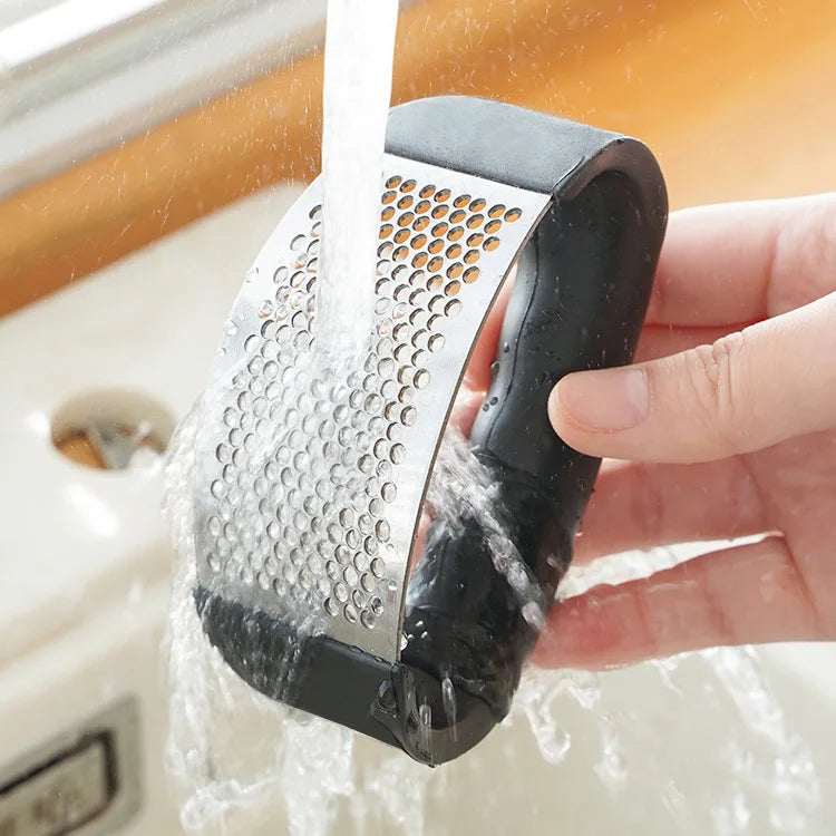 Manual garlic press rinsed under running water, perforated plate visible