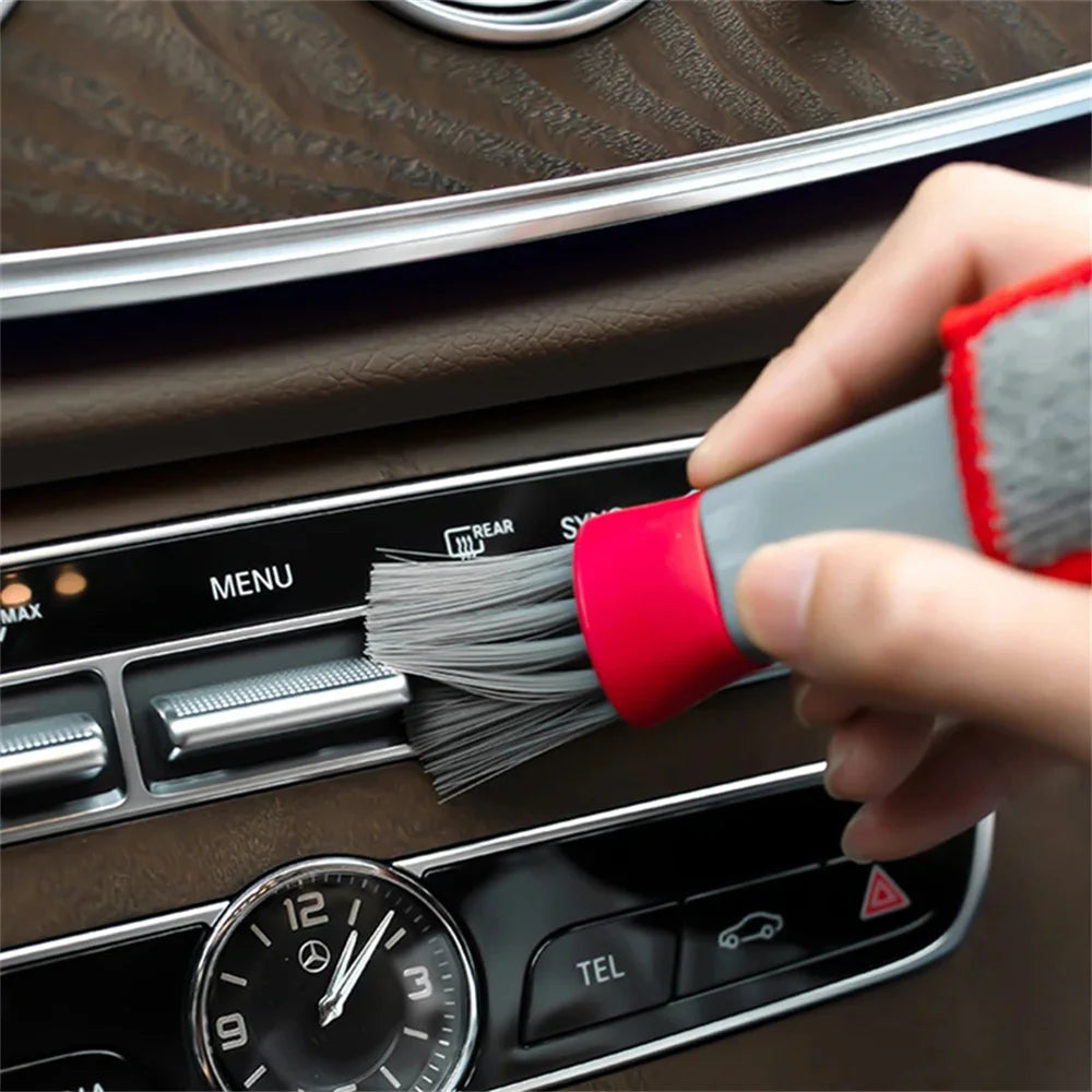 Car dashboard cleaning brush with gray bristles and red handle, held in hand