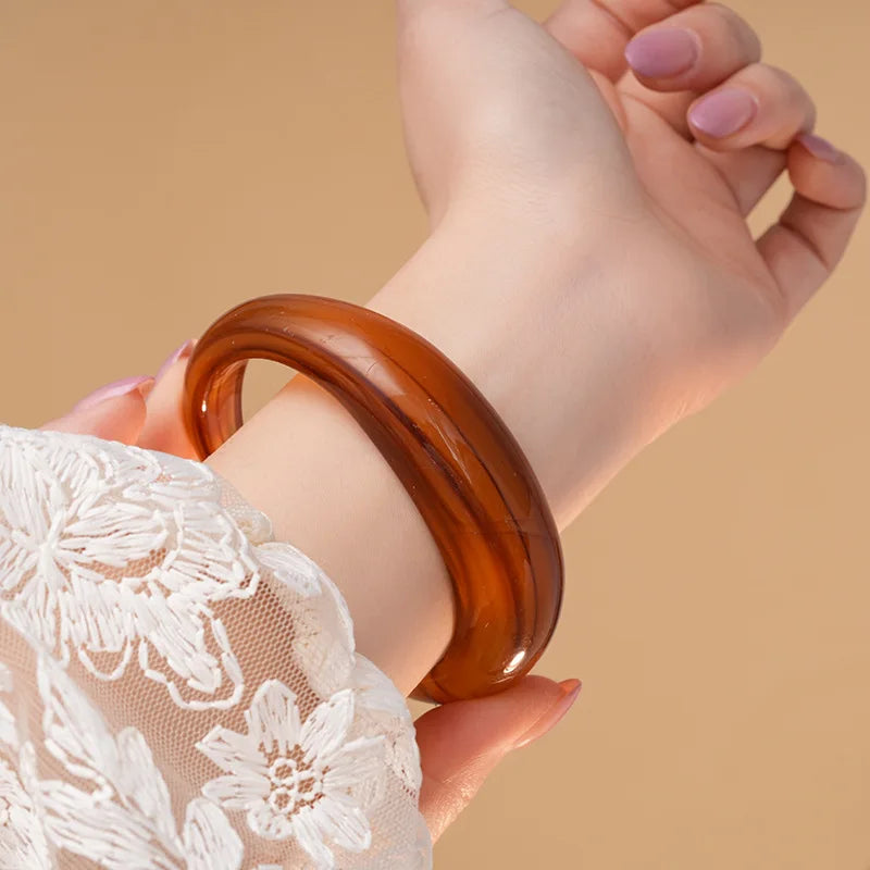 Shiny acrylic open cuff bangle in amber-brown worn on the wrist