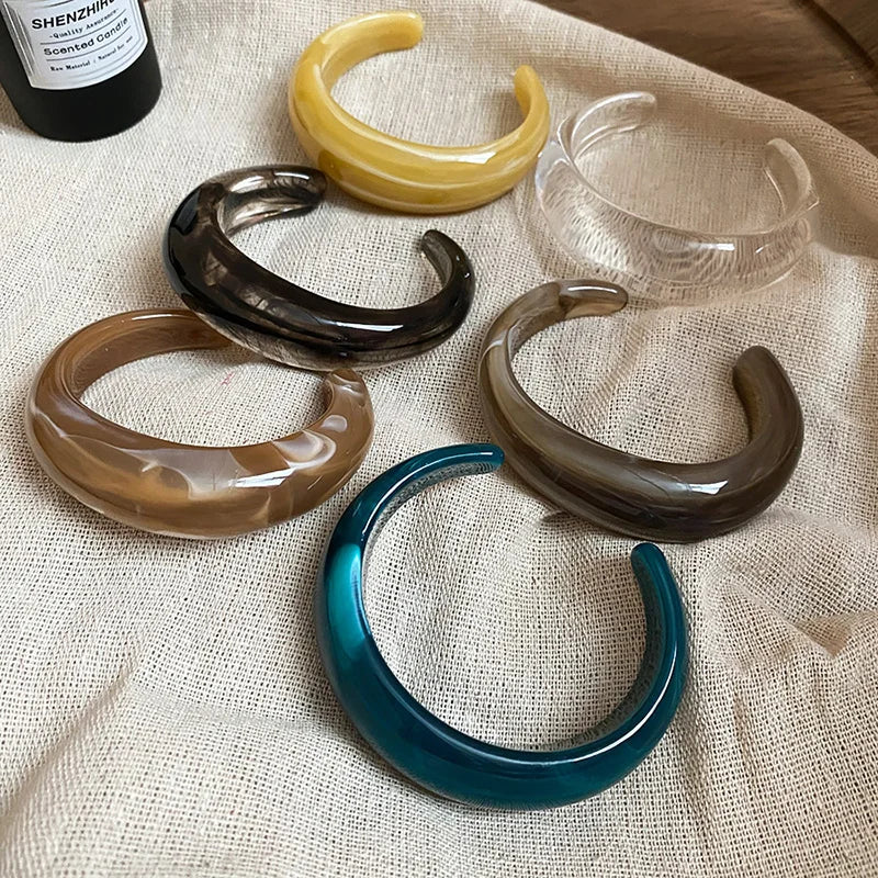 Assorted shiny acrylic open cuff bangles in yellow, black, clear, brown, and teal