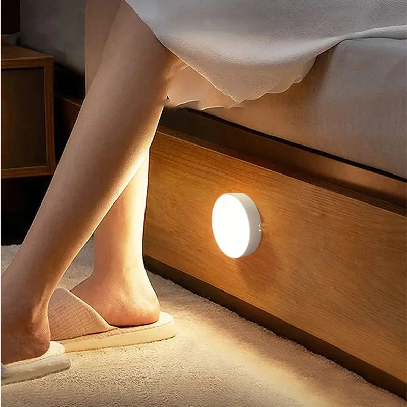 Round motion sensor night light glowing under a bed near the floor