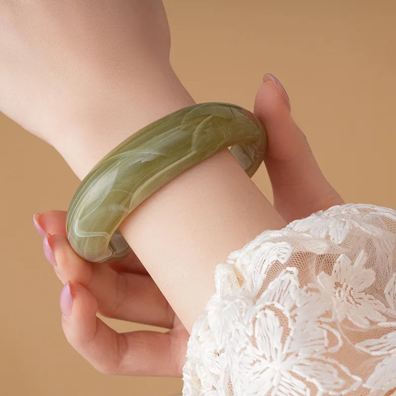 Translucent shiny acrylic open cuff bangle in light olive green on the wrist