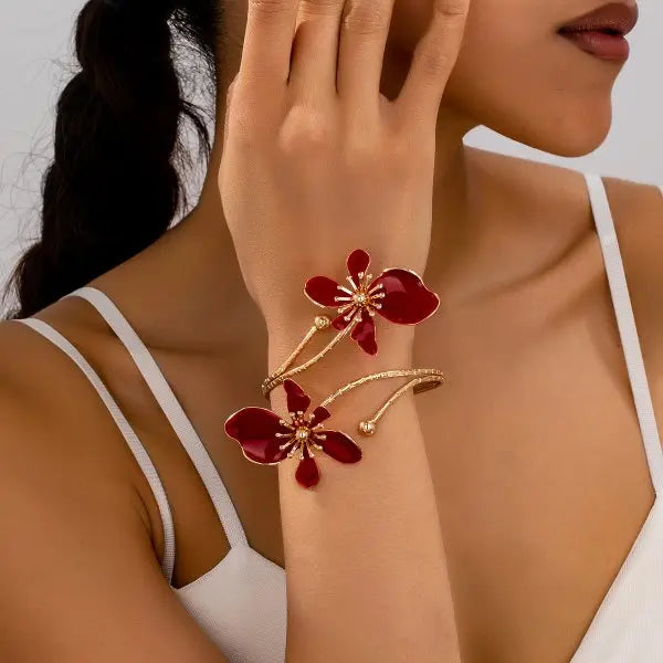 Gold-tone arm bracelet with red enamel flower charms and dangling bead details.