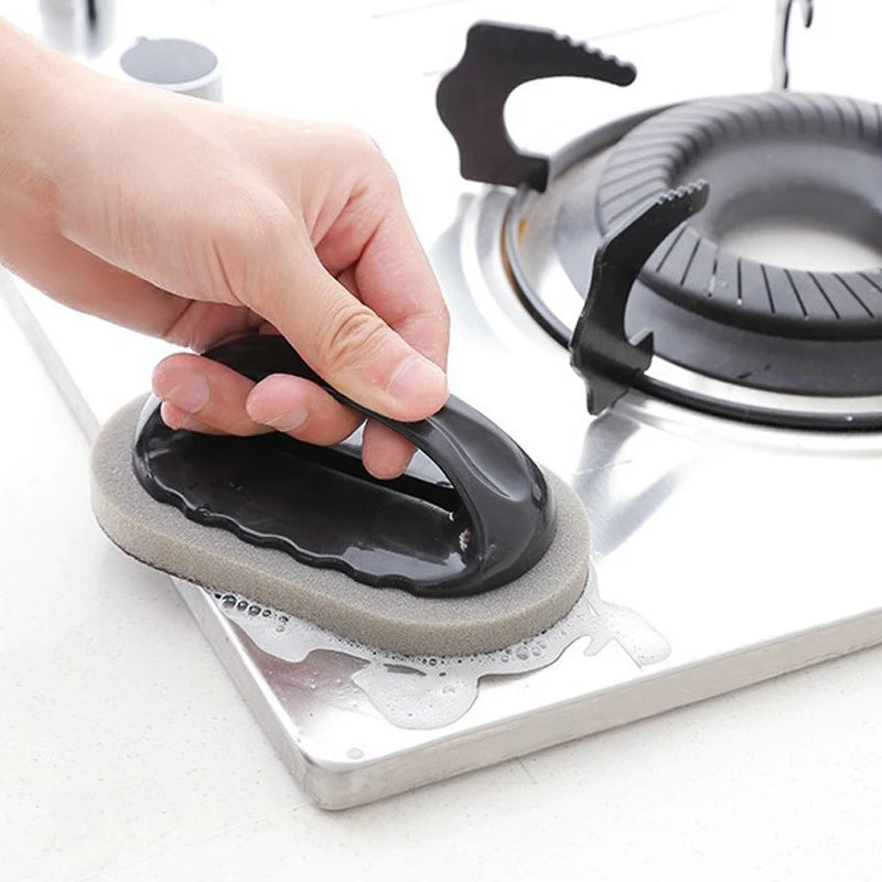 Kitchen cleaner brush with emery sponge pad and black handle on a stove