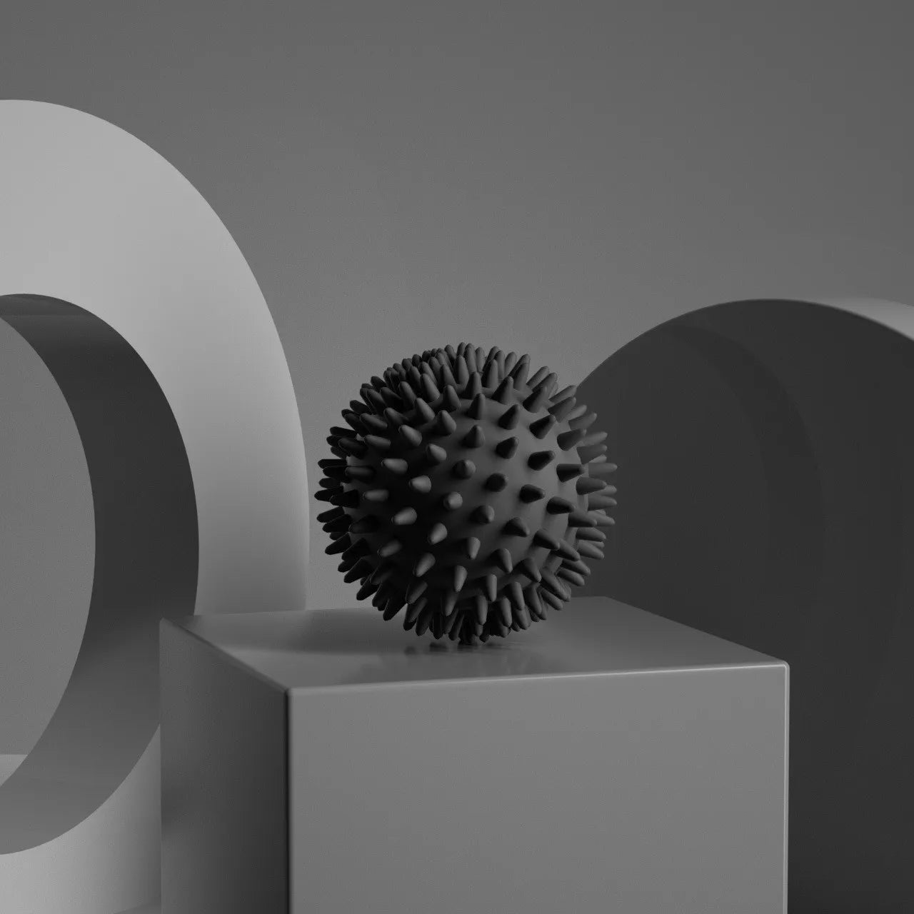 Black spiky fascia massage ball for muscle relaxation, shown on a gray block