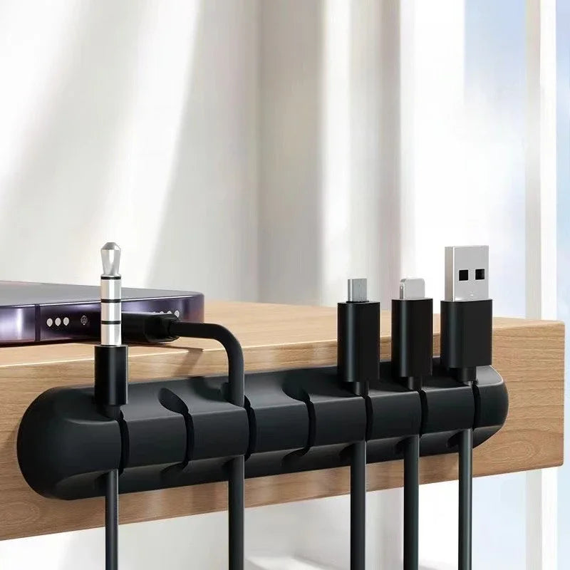 Black cable organizer snap clips on wooden desk holding several cables and connectors