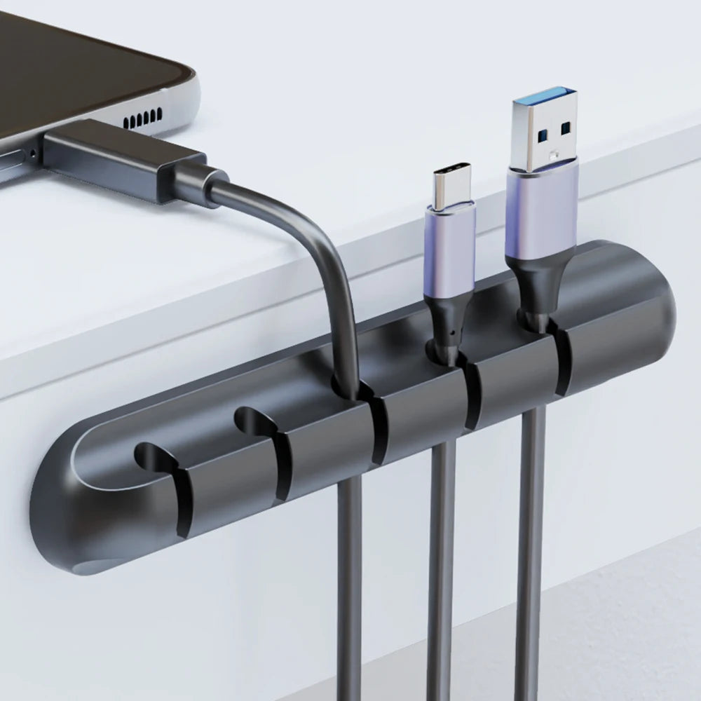 Black adhesive cable organizer clip holding multiple charging cables and USB plugs