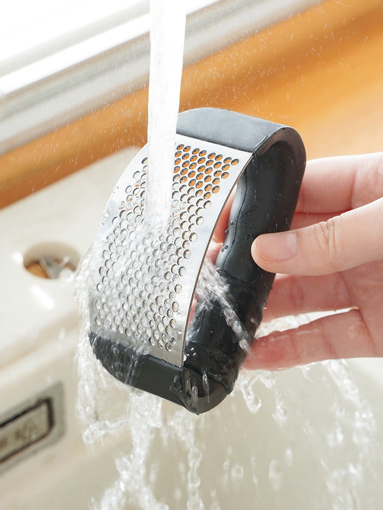 Stainless steel garlic press used over sink, showing crushed garlic juice