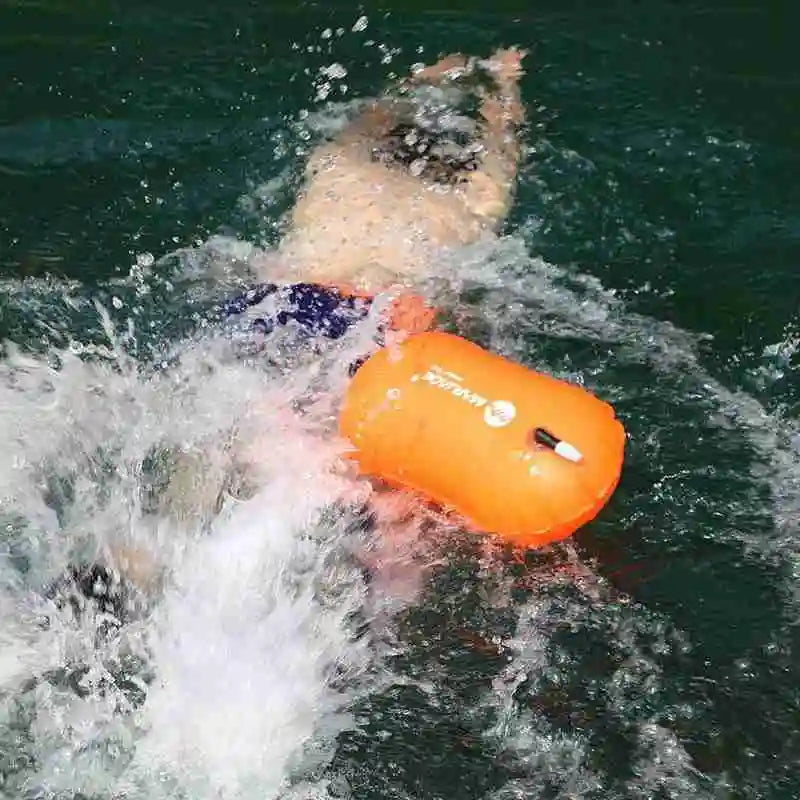 Inflatable swim buoy tow float in orange floating in open water with air valve